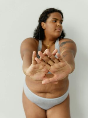 Confident plus size woman stretching in underwear, embracing body positivity indoors.