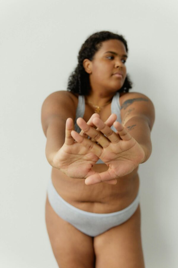 Confident plus size woman stretching in underwear, embracing body positivity indoors.
