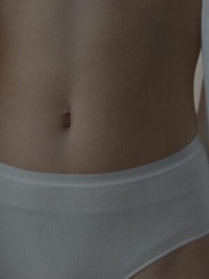 Intimate close-up image showcasing a woman's waist and belly button in white lingerie for fashion aesthetics.