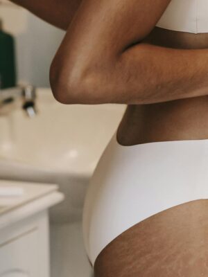Side view of crop unrecognizable ethnic female putting on underwear near pile of sanitary towels and washbasin
